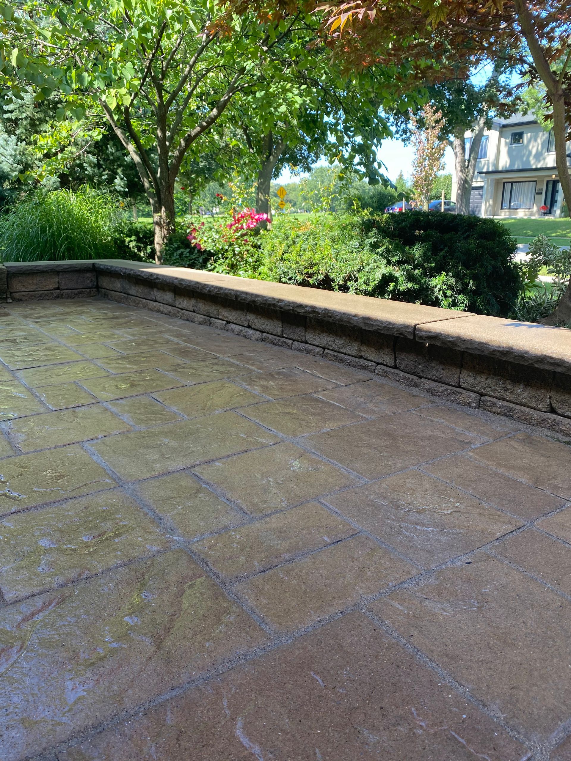 Stone patio with low wall, green foliage, trees, and a building in the background.