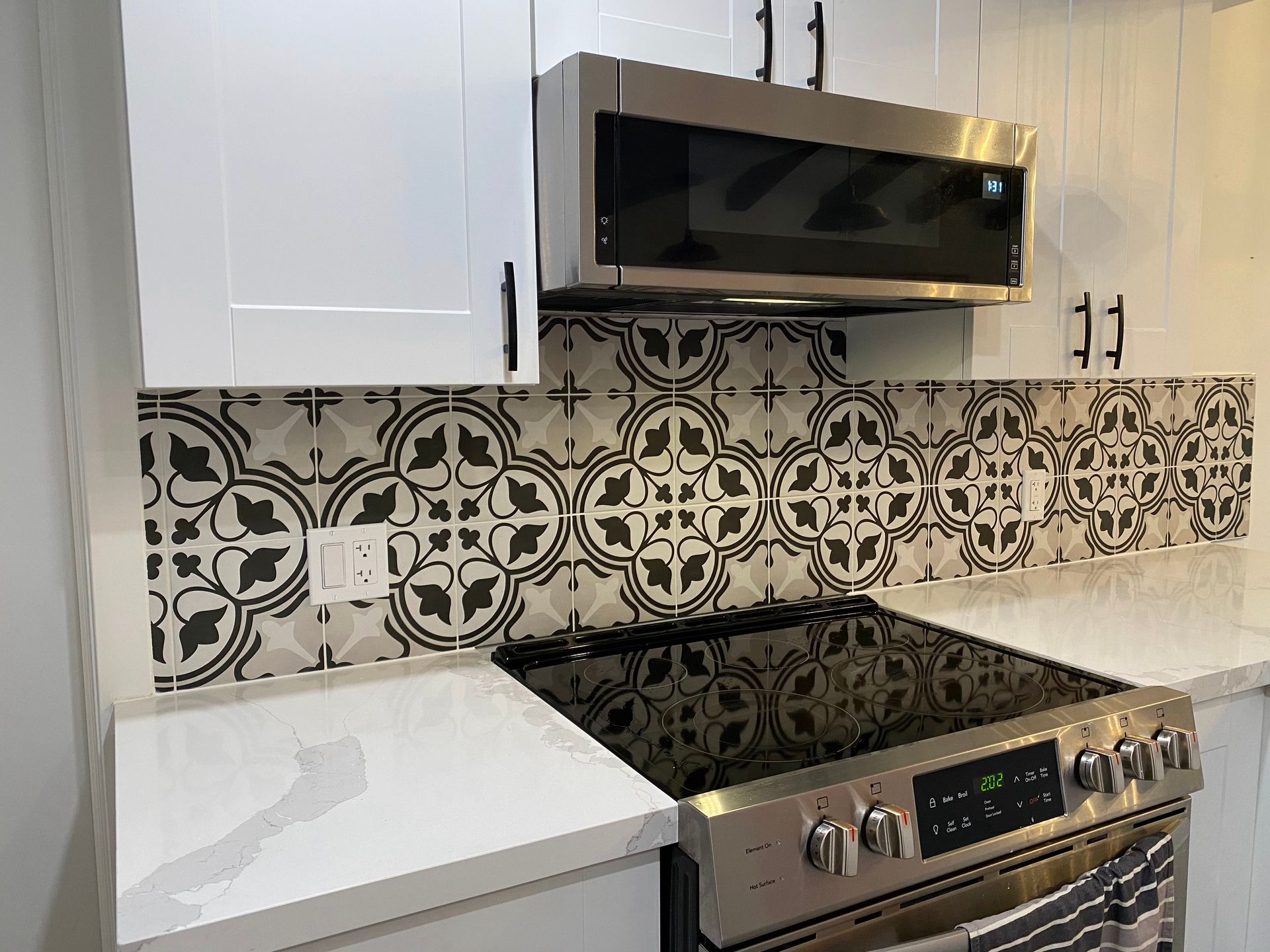 Kitchen with white cabinets, patterned backsplash, stainless steel appliances.