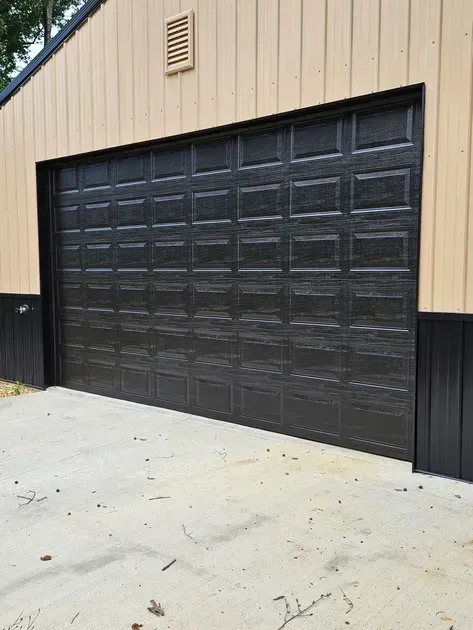 A black garage door is sitting in front of a tan building.