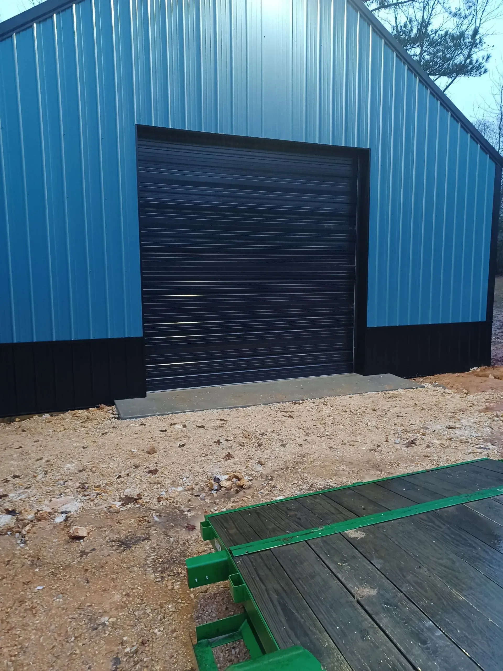 A blue building with a black garage door and a green trailer in front of it.