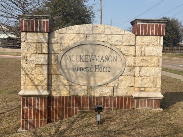 A stone and brick sign for Mulkey-Mason Funeral Home set against a grassy area under a clear sky.
