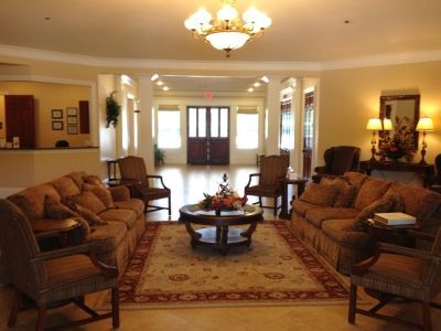 A spacious, warmly lit lobby featuring two brown sofas facing each other, armchairs, a central coffee table, and a rug.