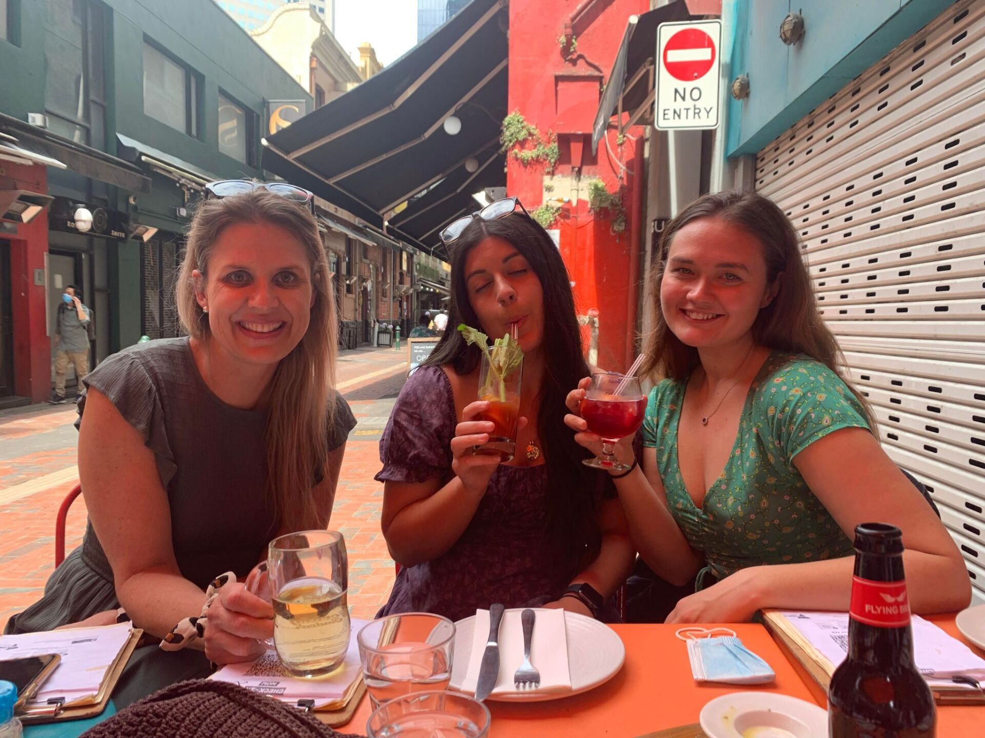 Three women are sitting at a table holding drinks.