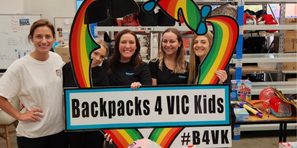 A group of women holding a sign that says backpacks 4 vic kids