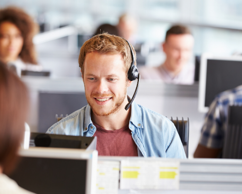 Man with headset smiling, working at computer in office setting.