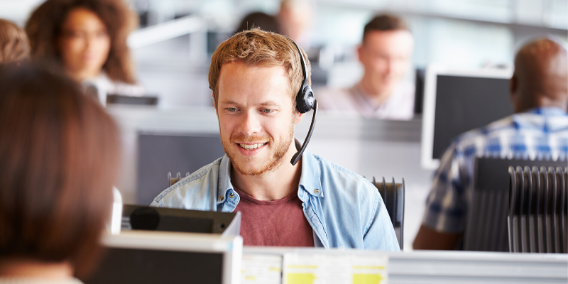 A man wearing a headset is sitting in front of a computer in a call center.