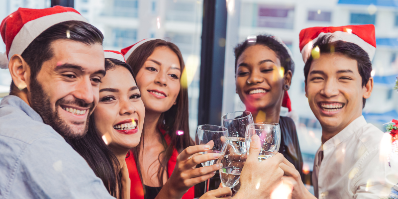 A group of people wearing santa hats are toasting with wine glasses at a christmas party.