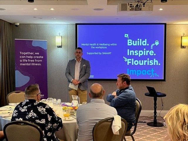 A man is giving a presentation to a group of people sitting at tables.