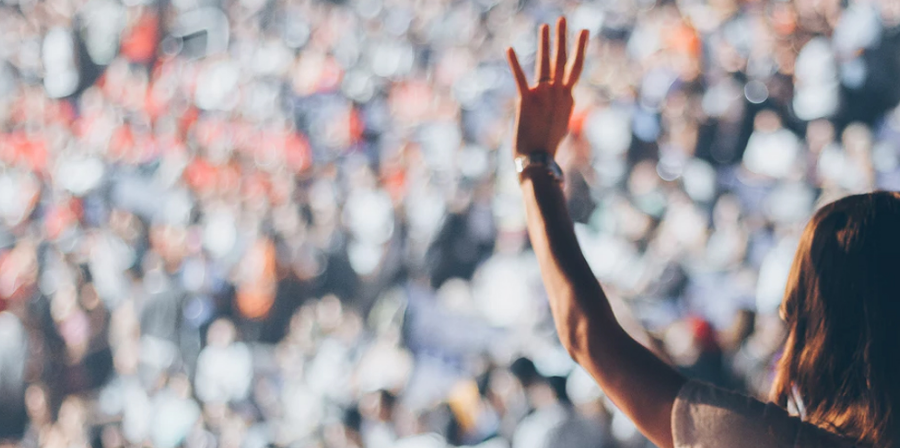 Person raises hand in front of a blurred crowd.