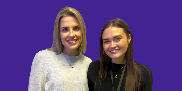 Two women are posing for a picture together on a purple background.