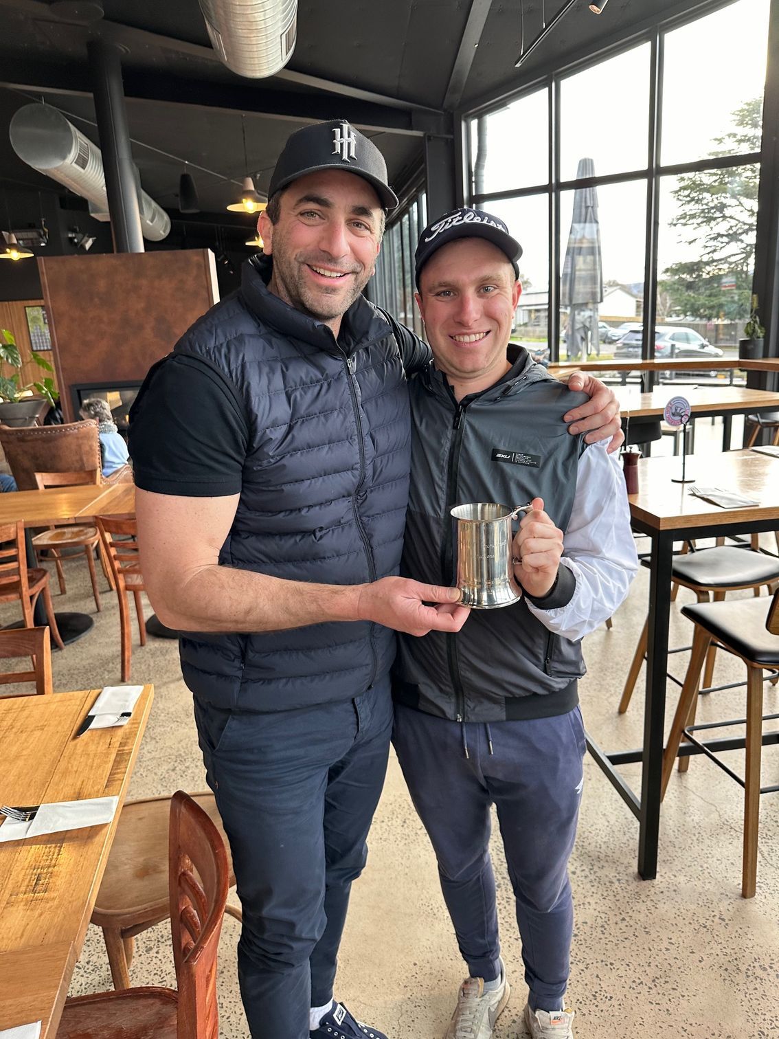Two men are standing next to each other in a restaurant holding a trophy.