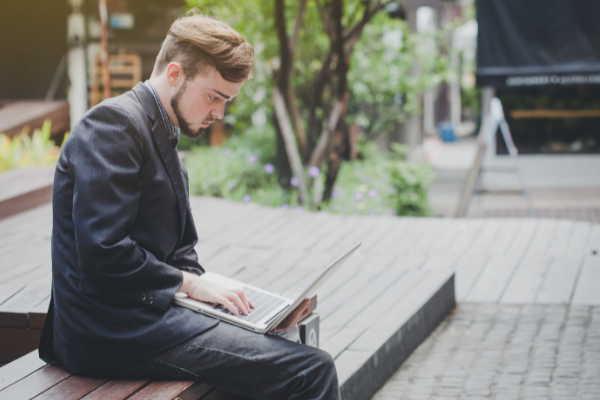 A man in a suit is sitting on a bench using a laptop computer.