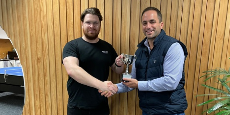 Two men are shaking hands while one of them is holding a trophy.
