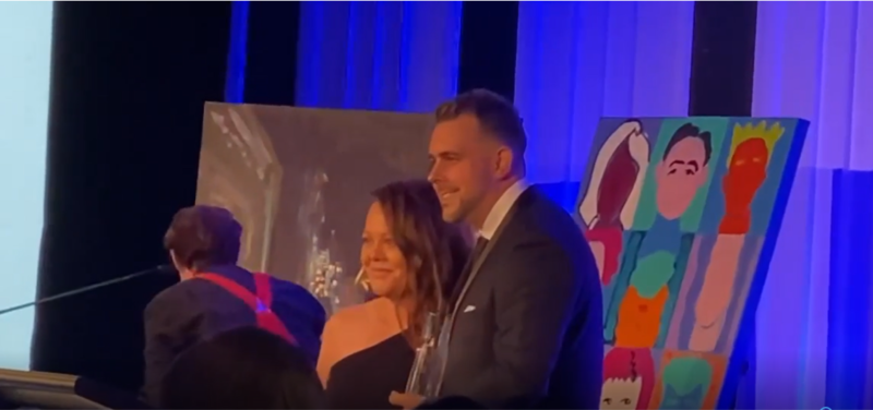 A man and a woman are standing next to each other on a stage in front of a painting.
