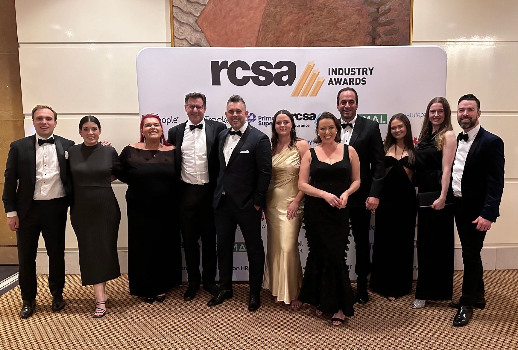 A group of people are posing for a picture in front of a wall that says rcsa.