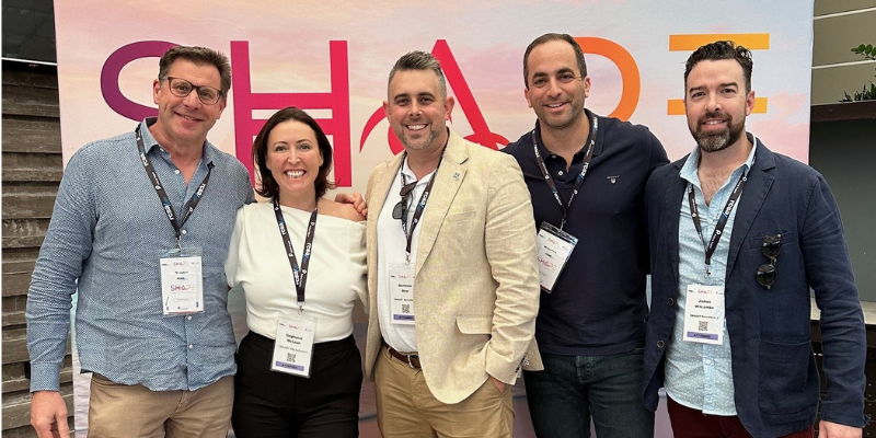 A group of people are posing for a picture in front of a sign that says shade.