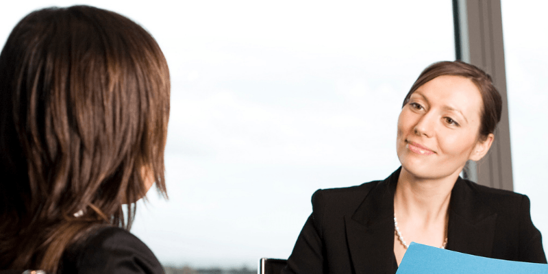 Two women are having a conversation in front of a window.