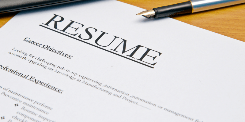 A resume is sitting on a wooden table next to a pen.