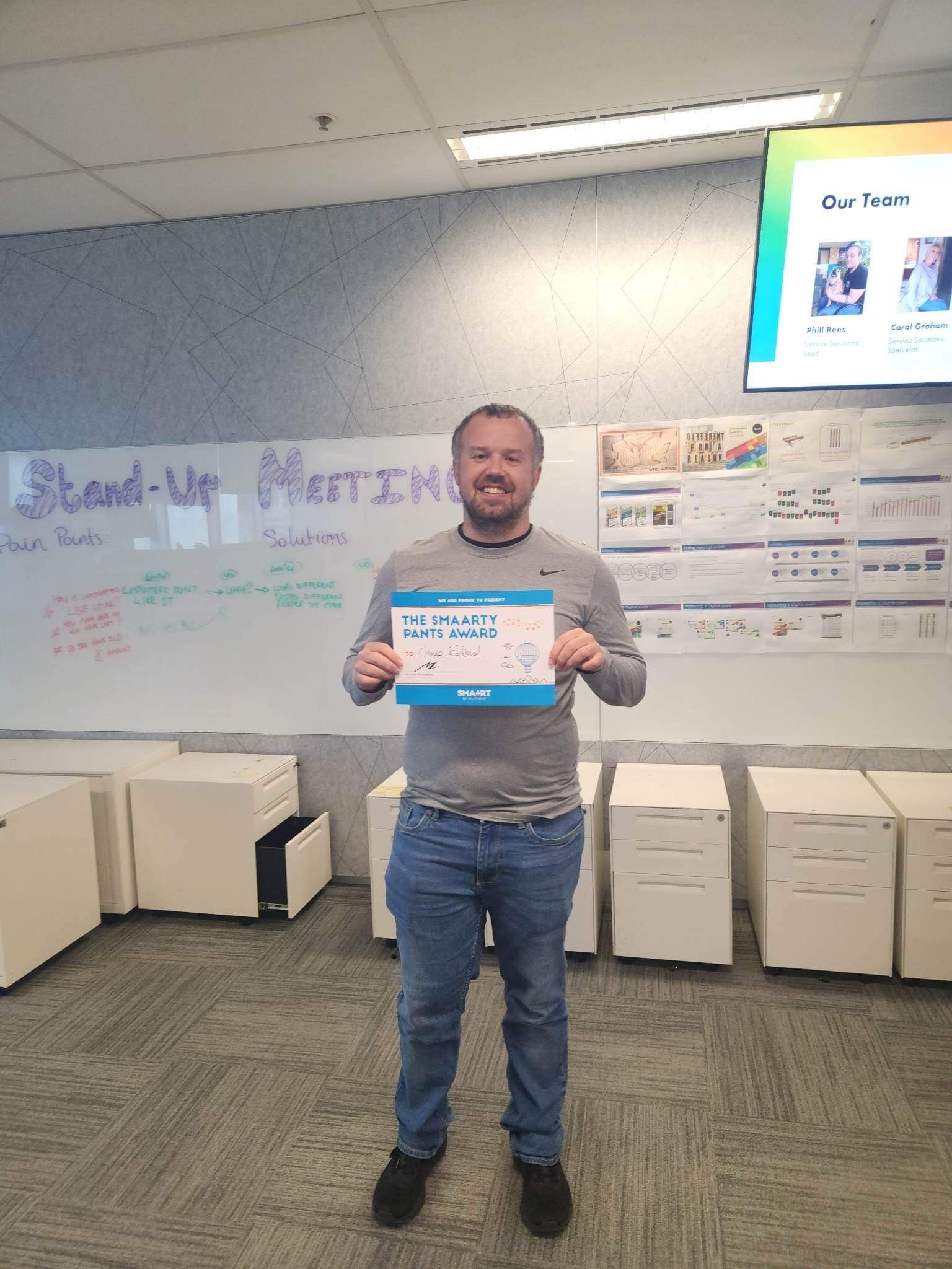 A man is standing in front of a white board holding a sign.