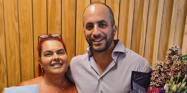 A man and a woman are posing for a picture in front of a wooden wall.