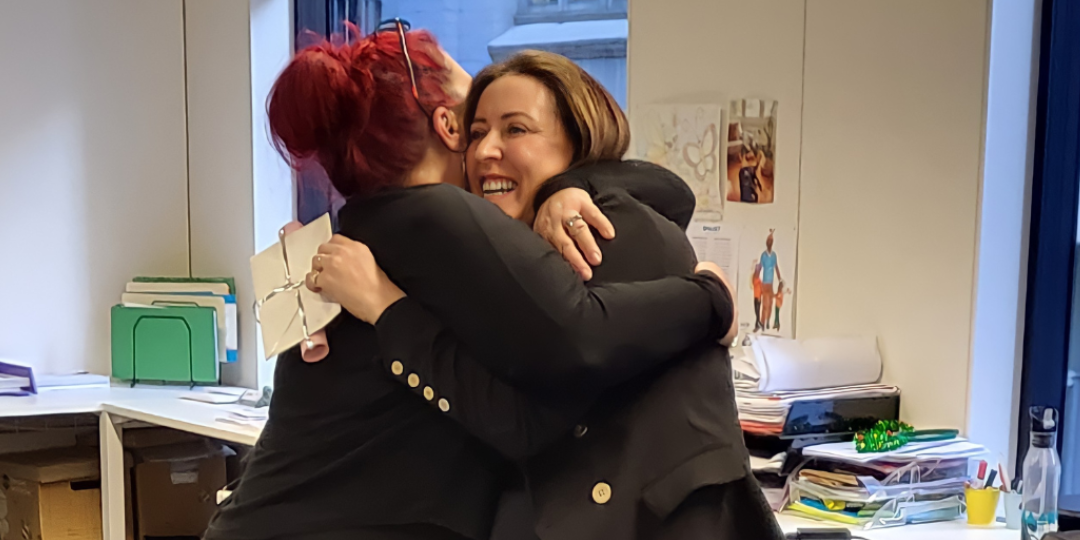 Two women are hugging each other in an office.