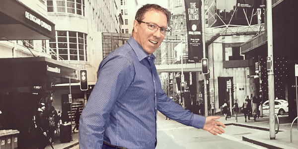A man in a blue shirt and glasses is walking down a city street.
