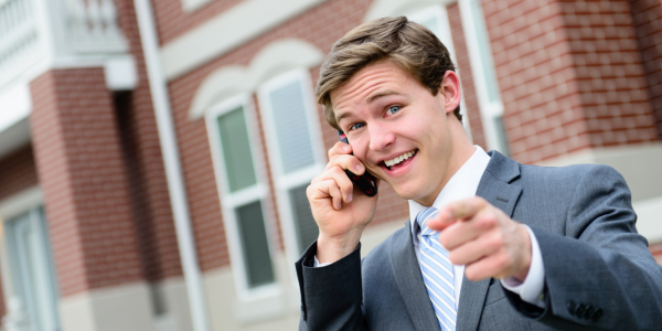 A man in a suit is talking on a cell phone and pointing at the camera.