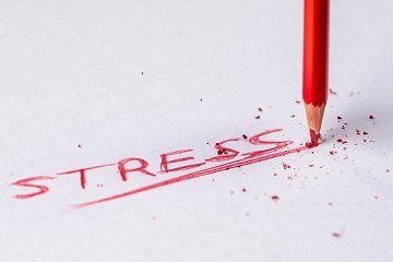 A red pencil is shaving the word stress on a piece of paper.