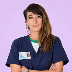 Donna in camice blu scuro con badge identificativo, braccia incrociate, su sfondo viola chiaro.