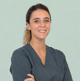 Persona sorridente in camice blu con le braccia incrociate su sfondo verde chiaro