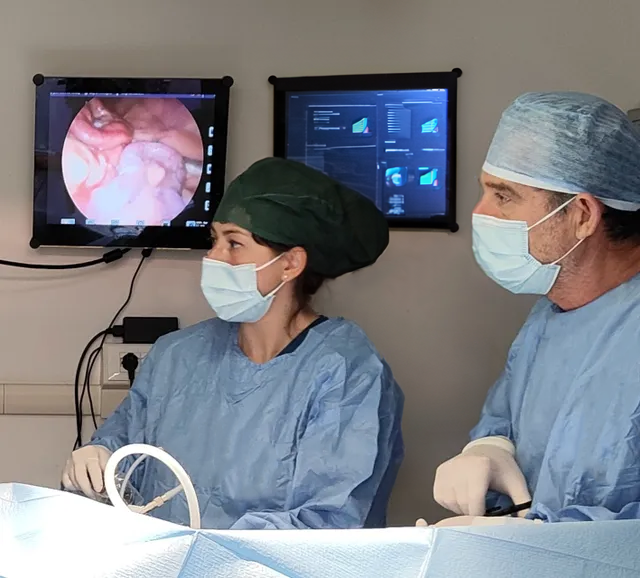 Personale medico in camice chirurgico osserva una procedura su dei monitor in sala operatoria.