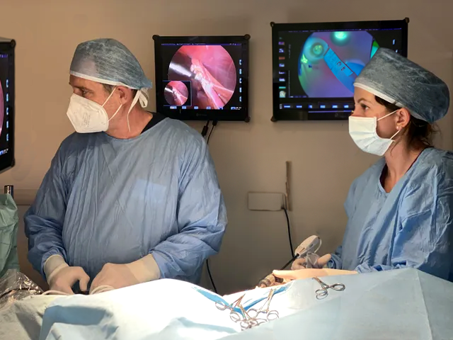 Personale medico in camici chirurgici blu e mascherine opera in una sala operatoria con monitor nelle vicinanze.