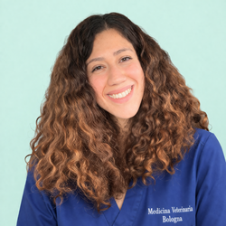Donna sorridente con i capelli ricci, che indossa una maglietta blu su uno sfondo verde menta chiaro.