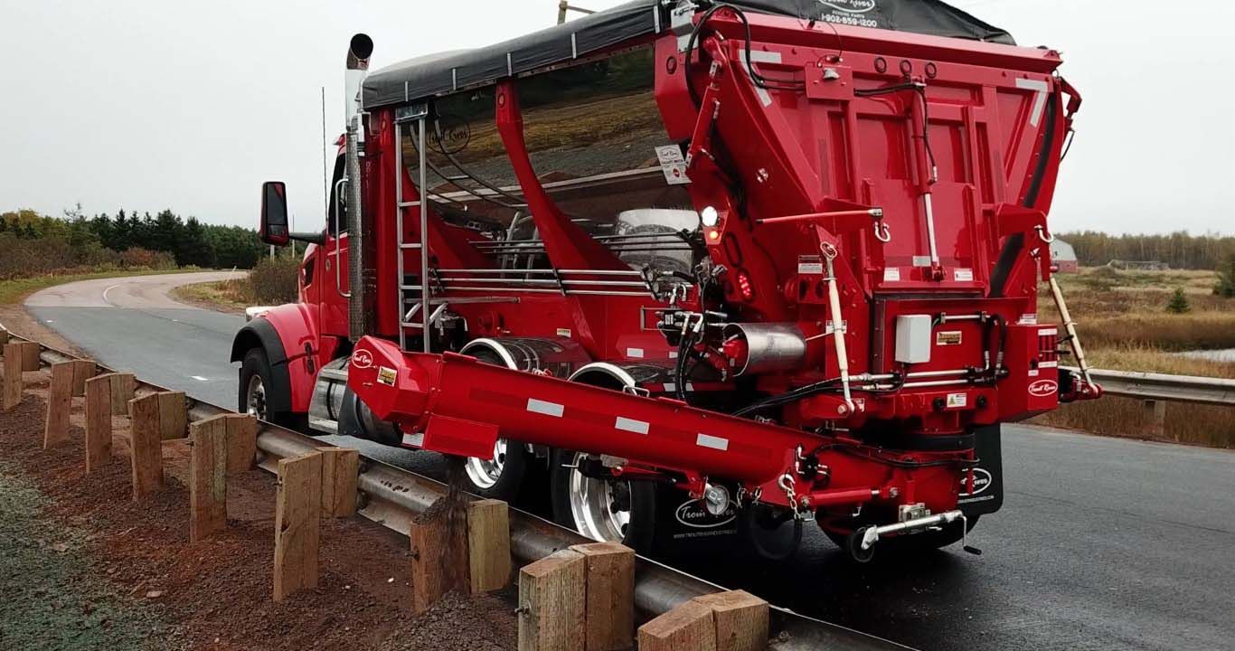 Trout River Industries truck-mounted live bottom auger dispensing gravel over a bridge guard rail 