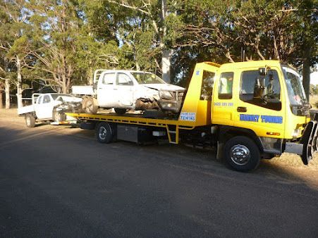 Yellow tow truck carrying a damaged white pickup on a road
