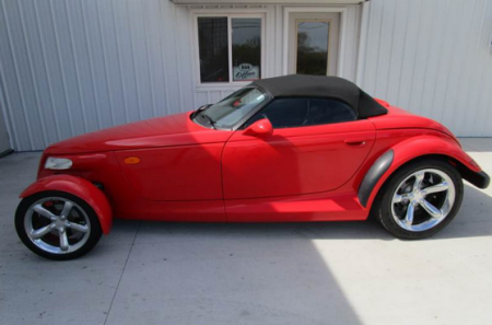 Red Plymouth Prowler convertible with black top, parked in front of a building.