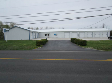 A storage facility with white doors, a paved driveway, and a sign on a cloudy day.
