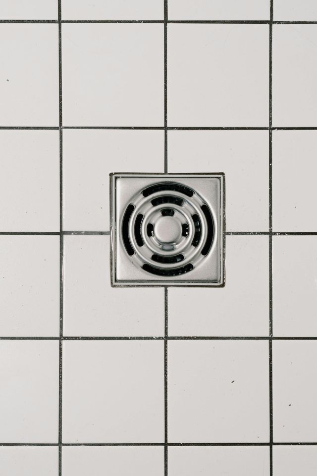 Square metal shower drain in white tiled floor.