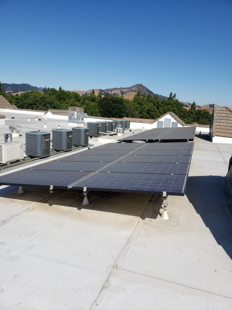 white commercial rooftop with air conditioning units; mountains in the background under a blue sky.