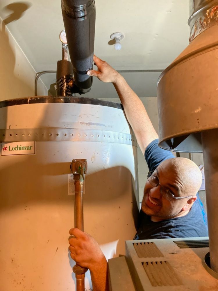 Man inspecting a hot water heater in a utility room. He touches the vent pipe with a concerned expression.