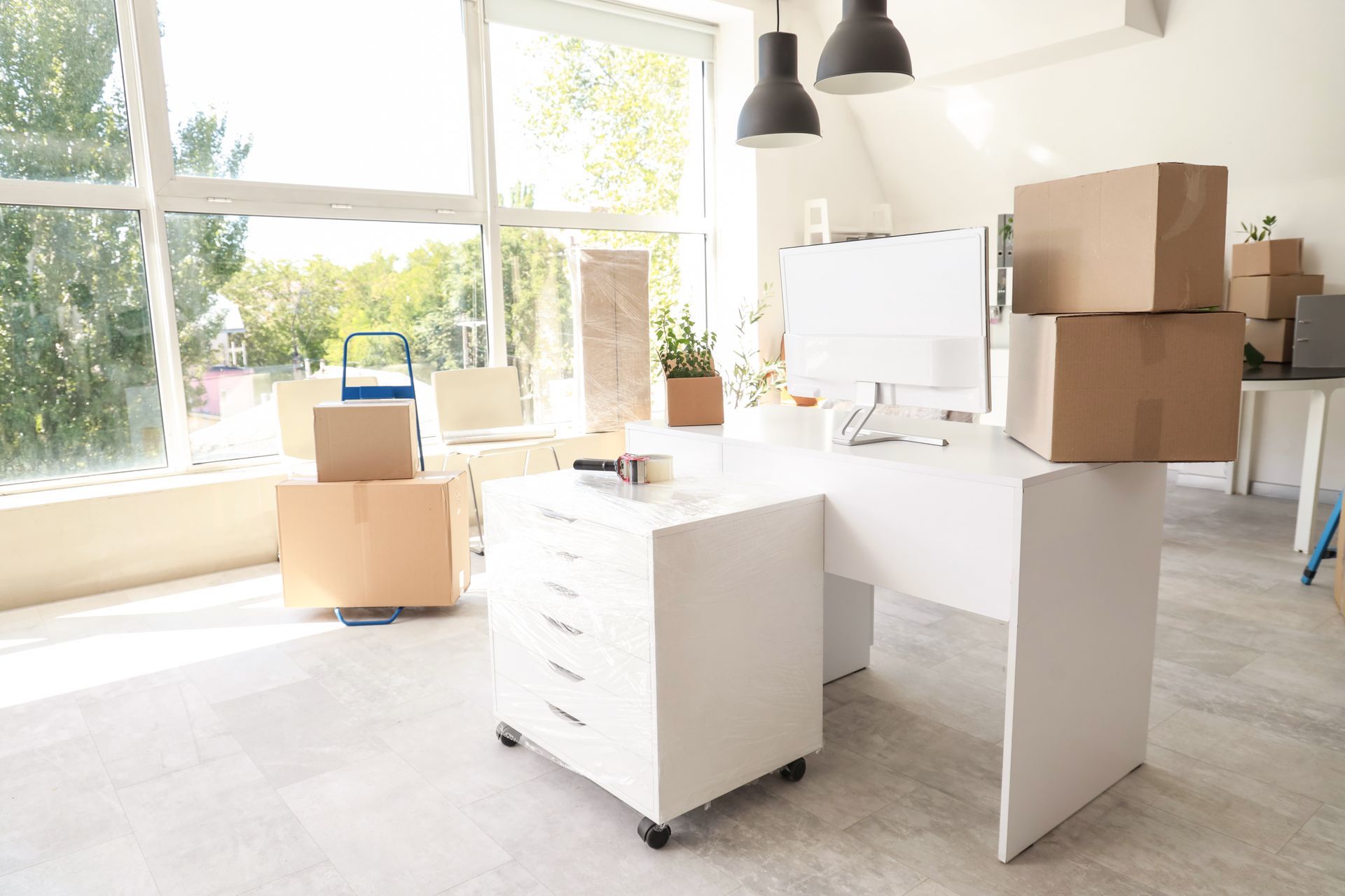 Bright office with moving boxes, white desks, and a large sunlit window