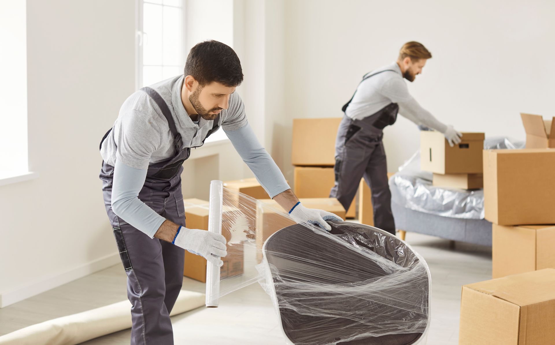 Two movers wrapping furniture in bubble wrap during a home move with boxes around them