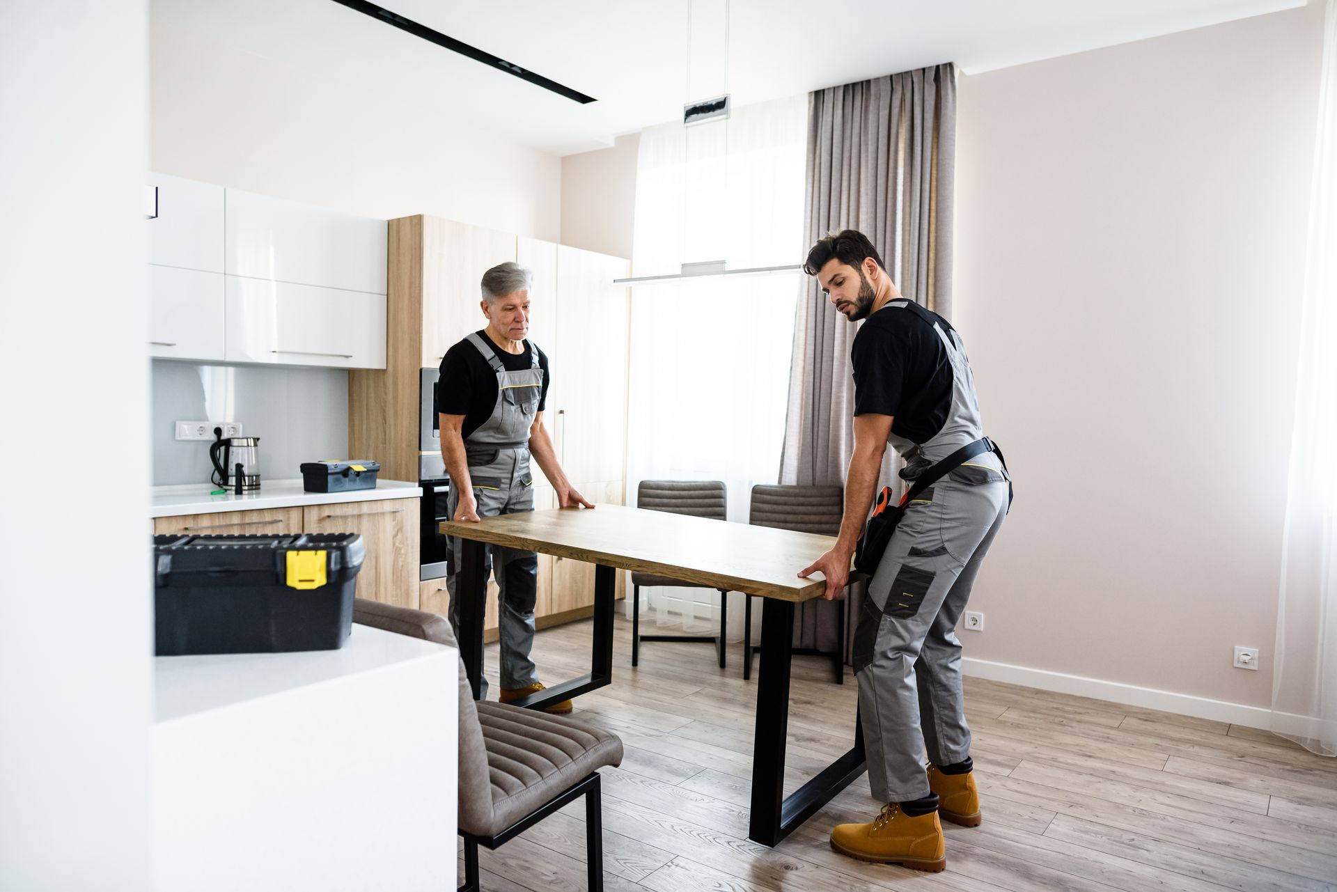 Two workers assembling a wooden table in a bright, empty room