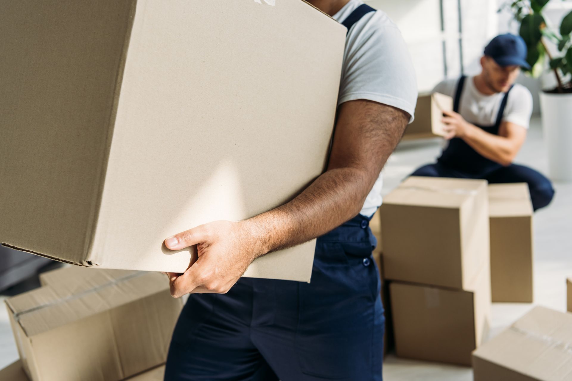 People carrying cardboard boxes during a move, with stacked boxes in the background.
