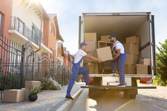 Two movers loading cardboard boxes into a truck outside a residential building.