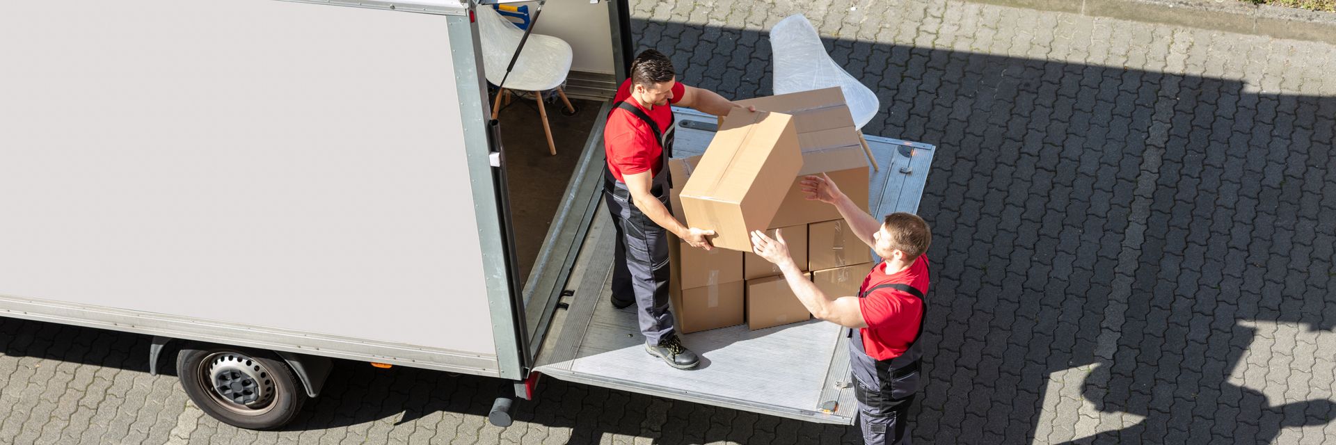 Two movers in red shirts loading cardboard boxes onto a truck ramp