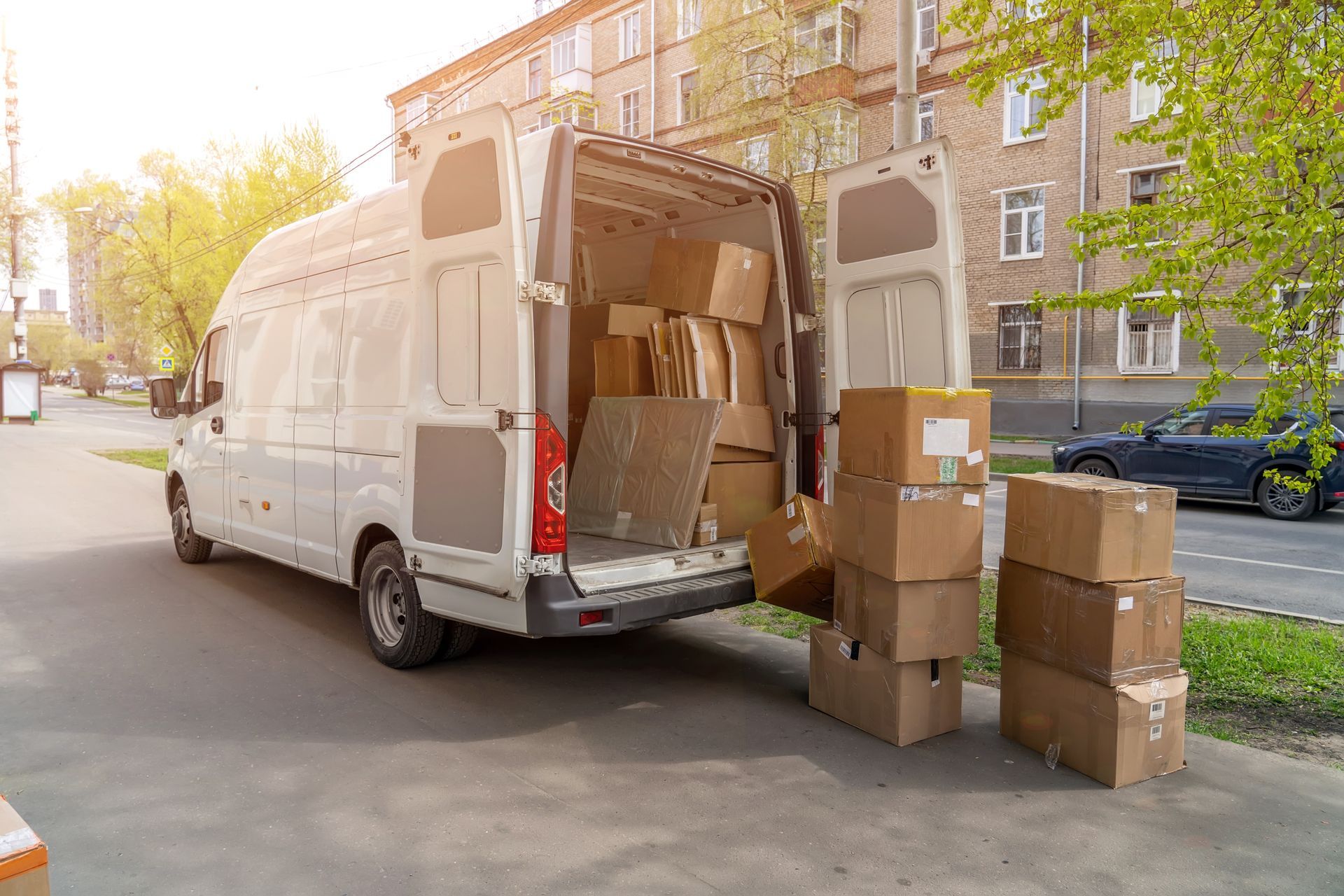 White cargo van being unloaded with stacked cardboard boxes on a city street.