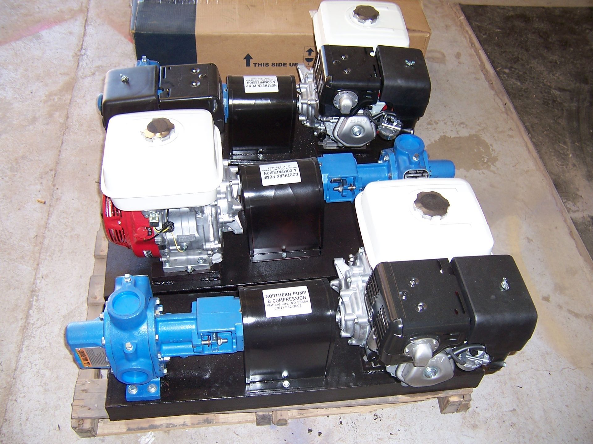 Four small industrial pumps/motors stacked on a pallet in a warehouse setting.