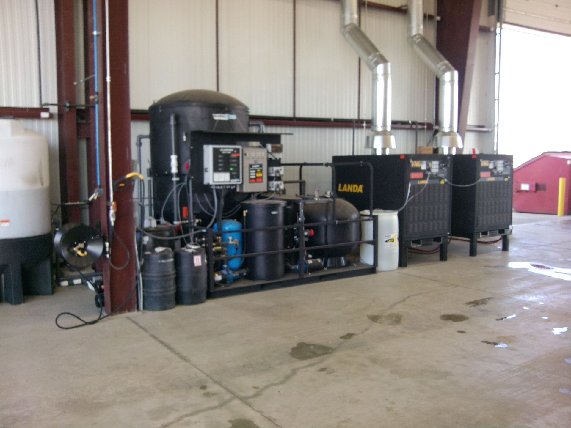Industrial equipment room with black tanks, pipes, and control panels in a warehouse-like space
