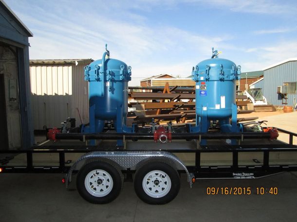 Blue industrial equipment mounted on a black trailer in an outdoor storage yard